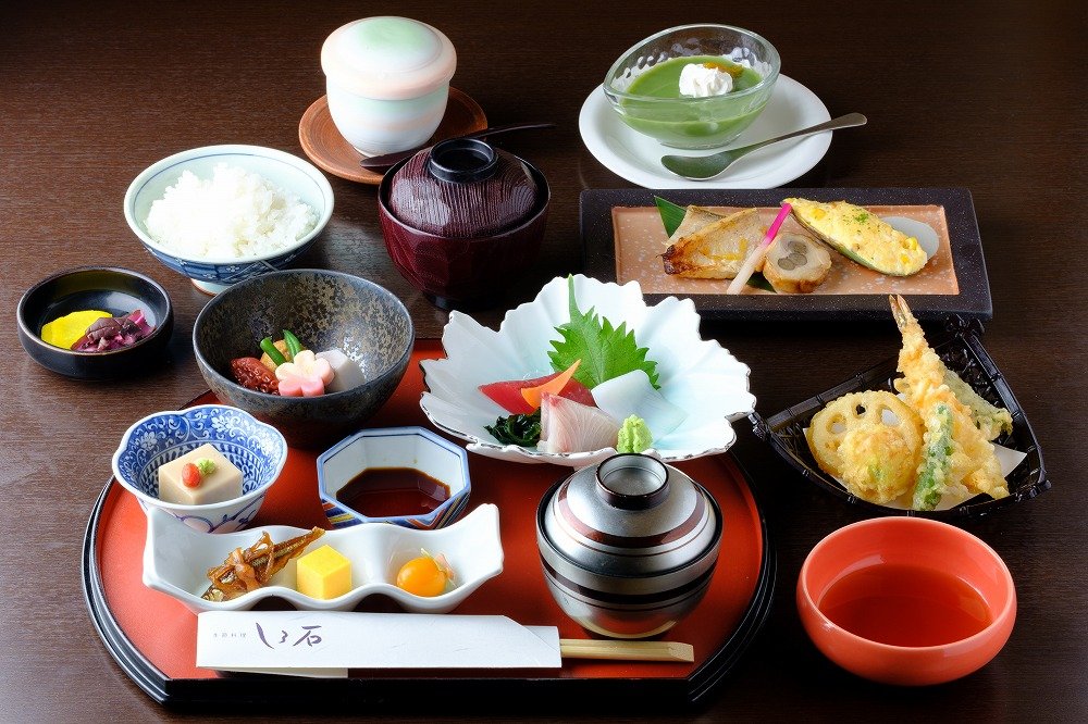食前酒と前菜、造り、焼き物が順に並ぶ昼の懐石コースをテーブル越しに撮った写真